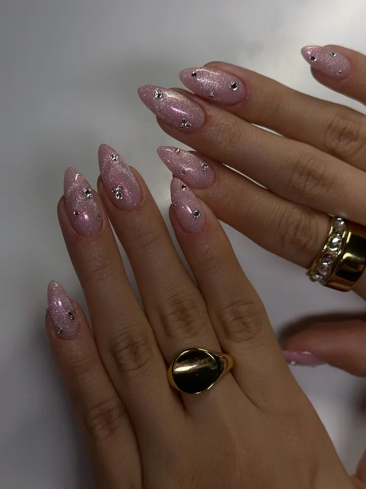 Pink cat-eye almond nails dotted with crystals, worn with gold rings