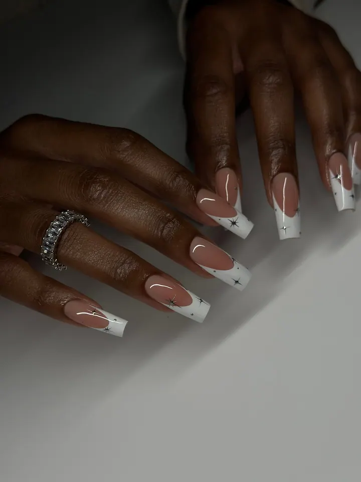Long square French tips in milky white with tiny silver star sparkles, on a grey table